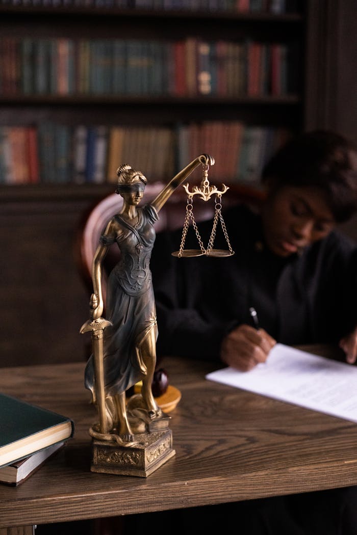 Close-up of Lady Justice figurine on a lawyers desk with books and documents.